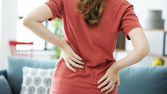 Woman holding lower back in pain before visiting Cary chiropractor